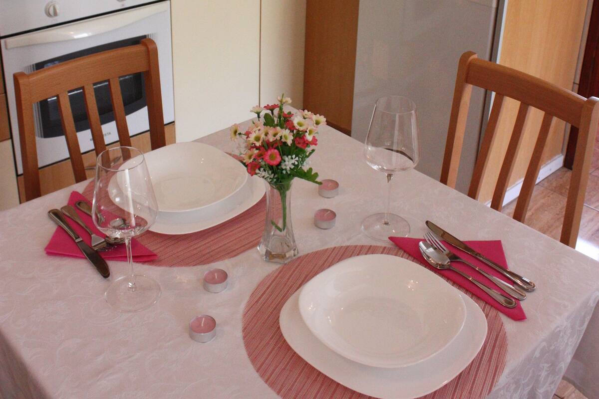 A kitchen with a dining table set for two, featuring a vase of flowers and wine glasses.