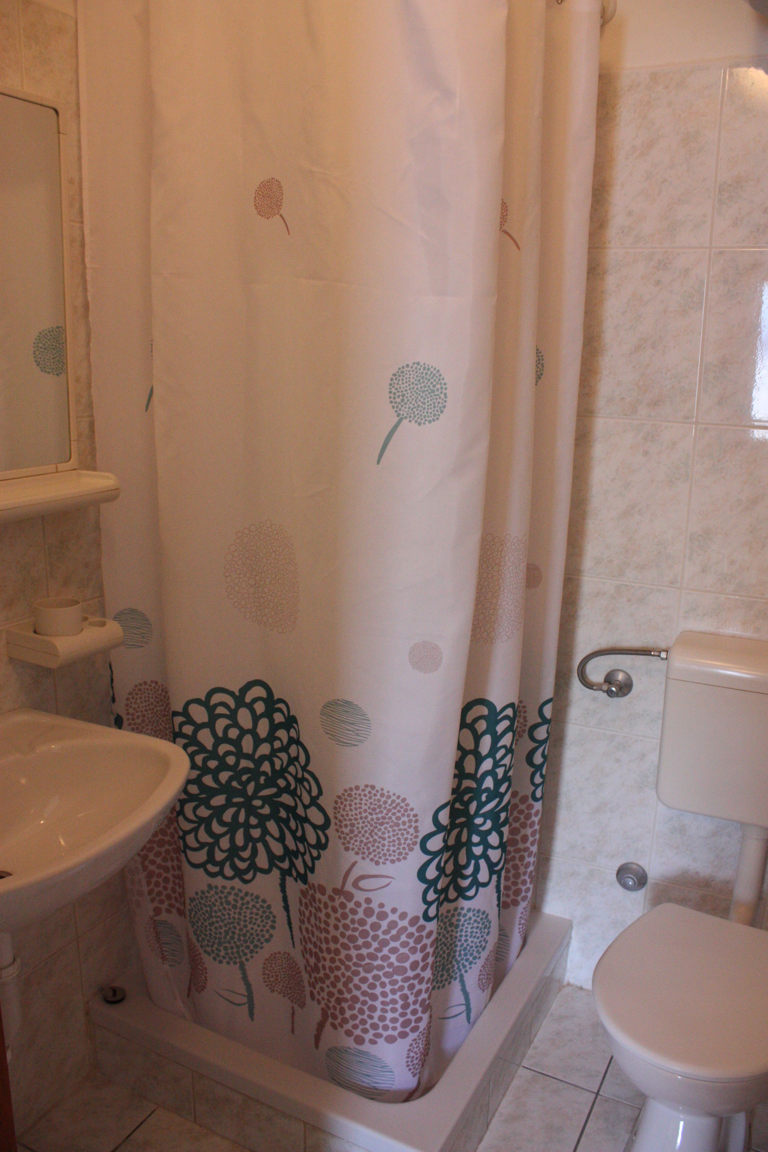 Een badkamer met douchegordijn met bloemenmotieven, toilet en wastafel.