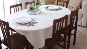 Ein Essbereich mit einem runden Tisch, Stühlen, einer weißen Tischdecke, einer Weinflasche und einem Gemälde an der Wand.