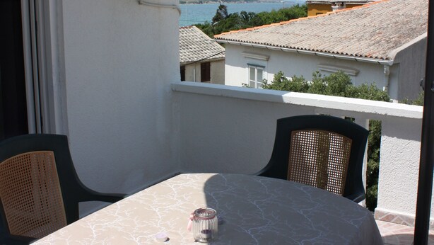 Ein Balkon mit Tisch und Stühlen, einer Klimaanlage und Blick auf Gebäude sowie ein Gewässer im Hintergrund.