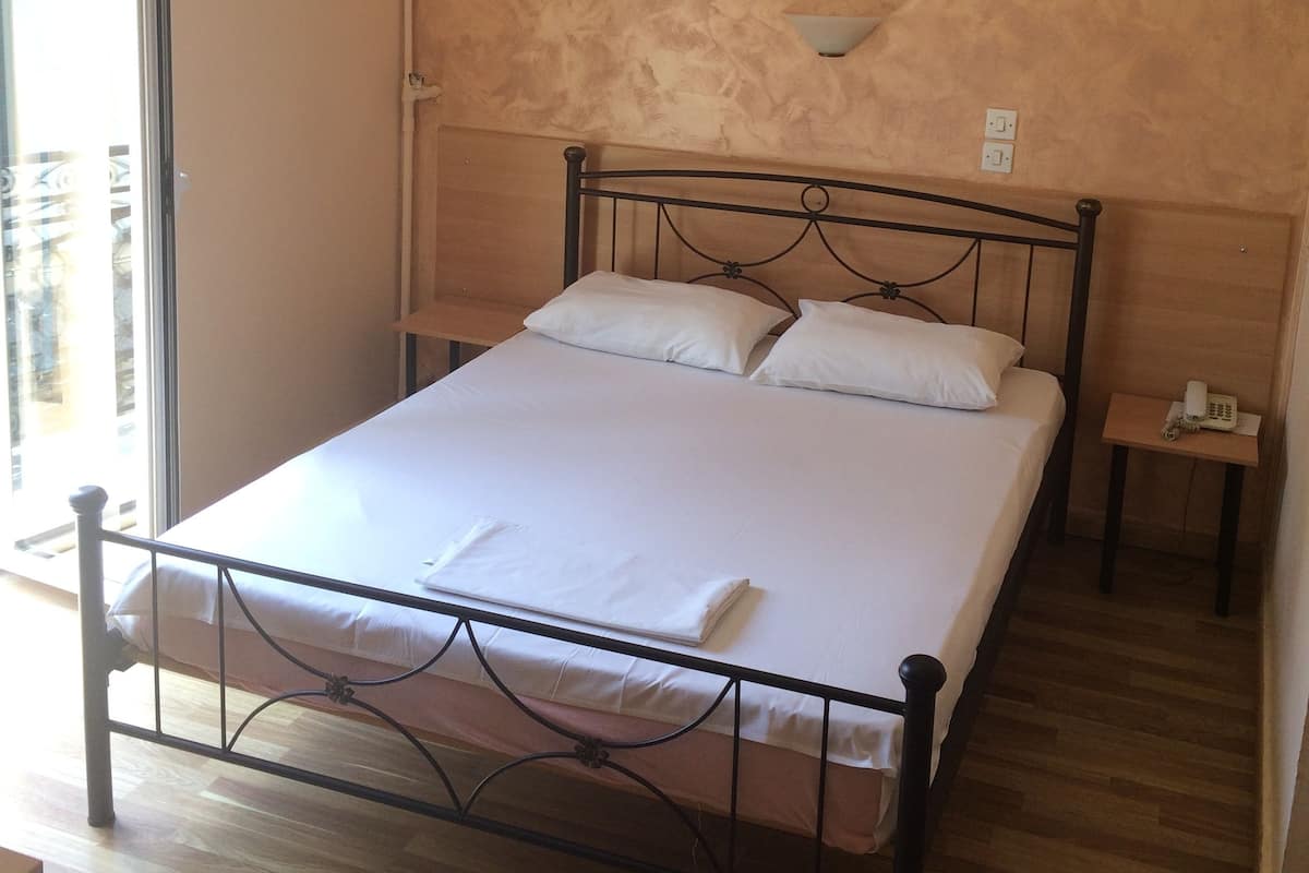 A bedroom with a bed, a painting on the wall, a bedside table with a phone, and a window with blinds.