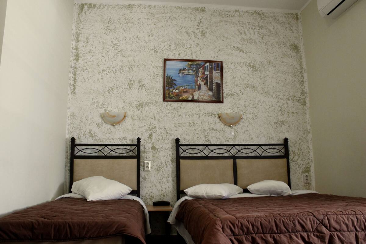 A room with two beds, a painting on the wall, and a small table.