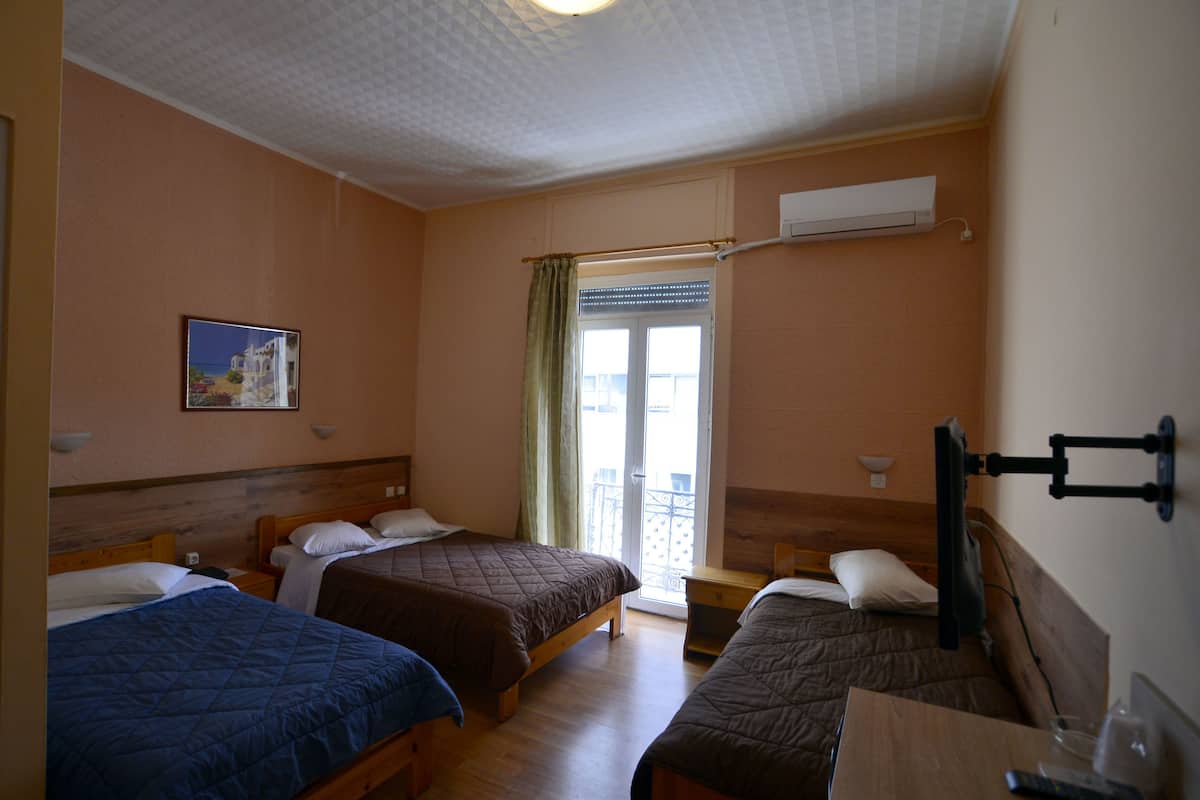 A hotel room with three single beds, a wooden desk, a TV, and a window with a view of the outside.