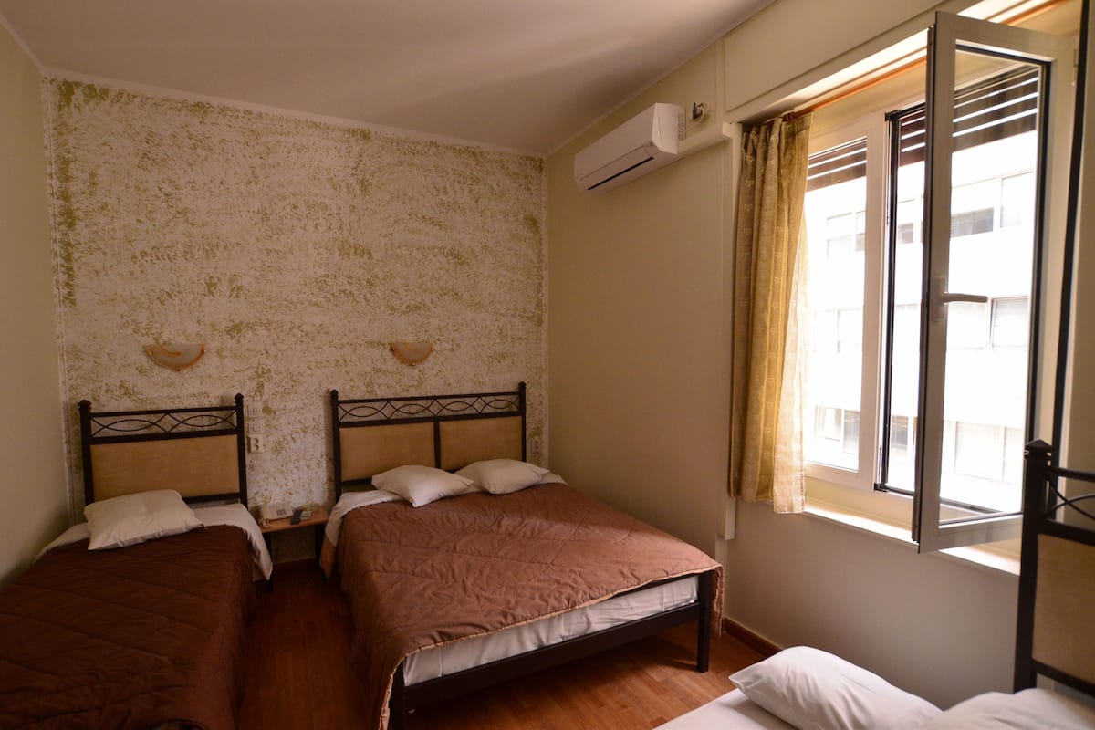 A room with two beds, a window with curtains, and an air conditioning unit on the wall.