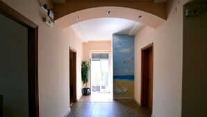 A hallway with a tiled floor, a ceiling with recessed lighting, and a mural on the wall depicting seagulls flying over the ocean. - Hotel Electra (Piraeus)