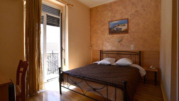 A bedroom with a bed, a chair, a nightstand, and a painting on the wall. - Hotel Electra (Piraeus)