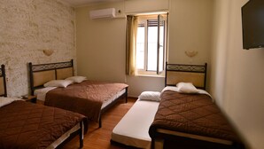 A room with three single beds, a window with curtains, an air conditioning unit, and a flat-screen TV mounted on the wall. - Hotel Electra (Piraeus)