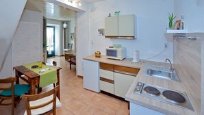 Een compacte keuken met een magnetron, spoelbak en een klein aanrecht. Er is een eettafel met stoelen en een groene tafelkleed.