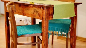 Een houten eettafel met een groene tafelkleed, een stoel met een blauw kussen, en een geel drankje op de tafel.
