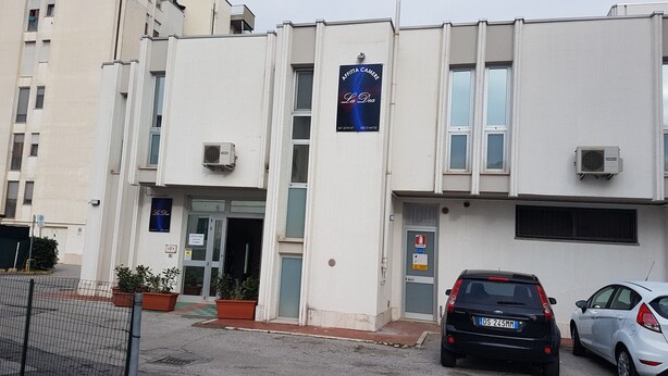 Un edificio con un cartel que dice "AFRITA CAMERE La Dea" y un estacionamiento con dos coches.