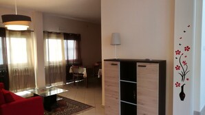 Una sala de estar con un sofá rojo, una mesa de centro de vidrio, un aparador de madera y un comedor con mesa y sillas.