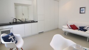 A modern kitchen with a sink and kettle, a white sofa with patterned cushions, and a chair with a blue cushion. - Boutique Apartments Palcic Palace (Pag)