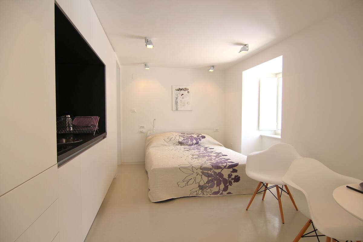 Quarto moderno com uma cama, uma cadeira branca e uma janela.