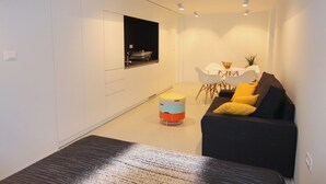 A modern living room with a black sofa, a small round table, and a white dining table with chairs. - Boutique Apartments Palcic Palace (Pag)