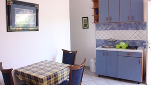Een kleine keuken met een eethoek, voorzien van een geruit tafelkleed, houten stoelen en een betegelde spatwand.
