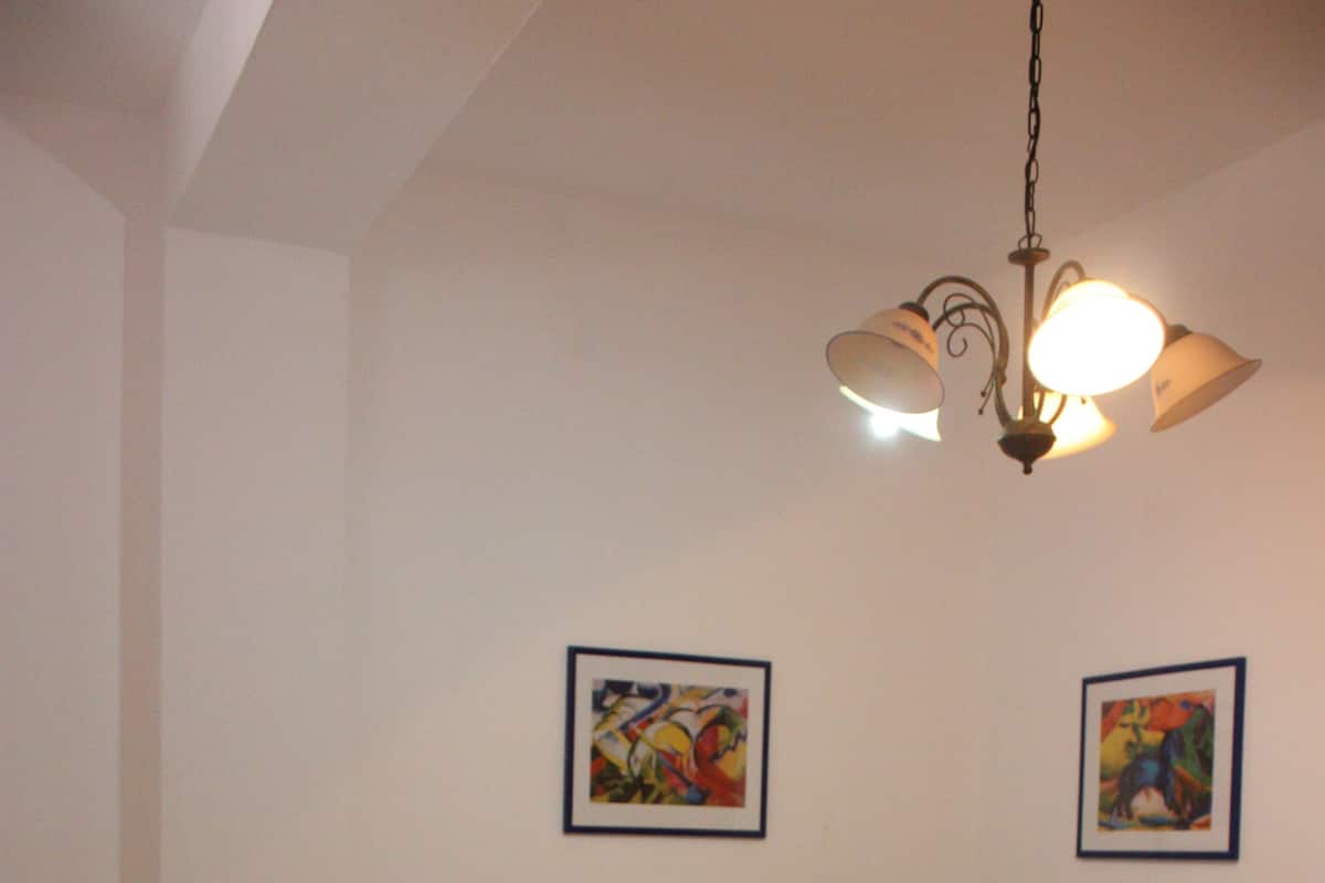 A bedroom with a bed, two pillows, a nightstand with a lamp, and two framed pictures on the wall.