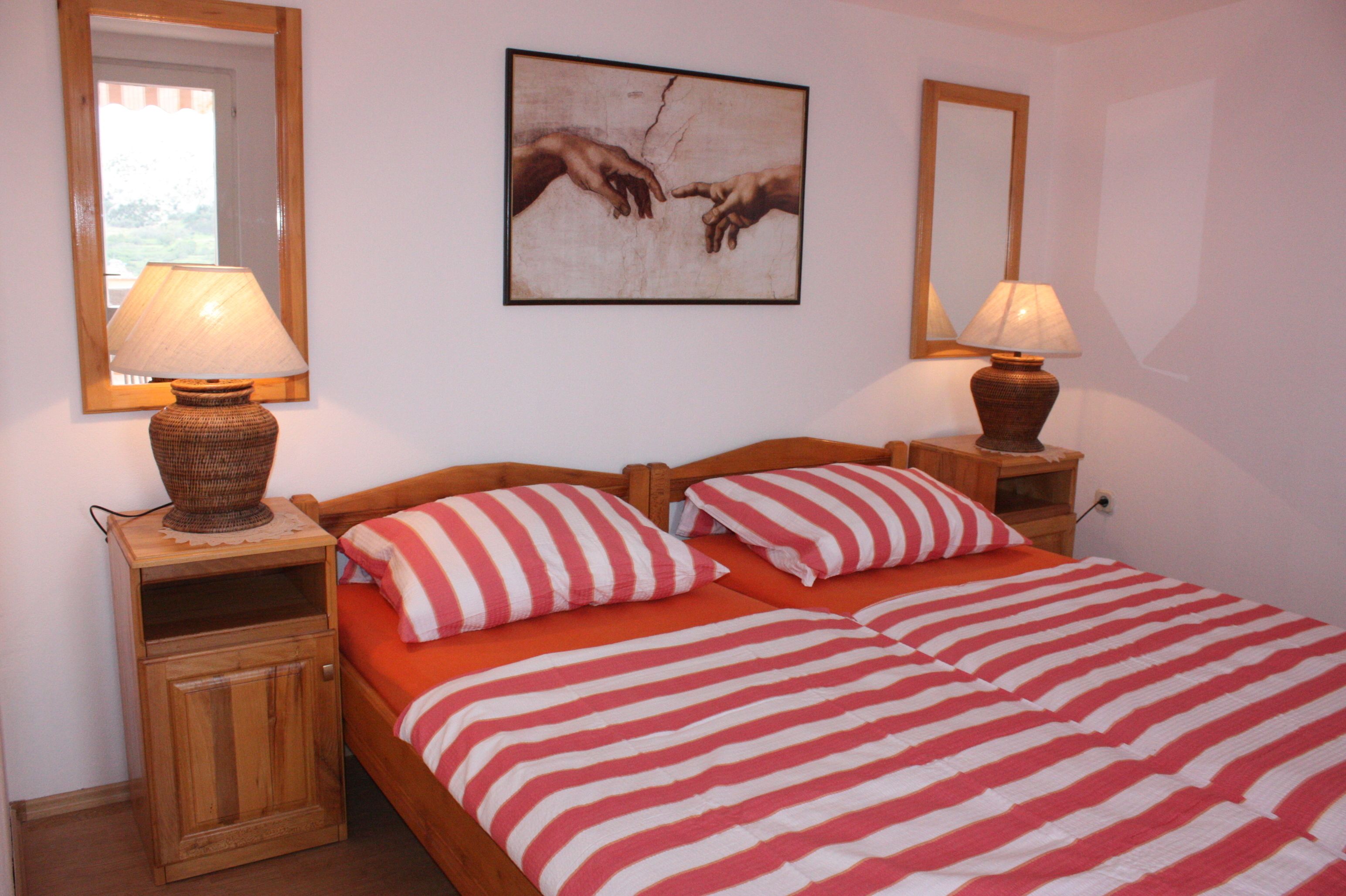 A double bed with red and white striped bedding, two bedside tables with lamps, and a framed artwork on the wall.