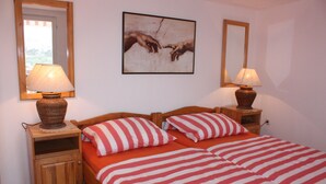 Een tweepersoonsbed met rood-wit gestreepte beddengoed, twee nachtkastjes met lampen, en een lijstwerk aan de muur.