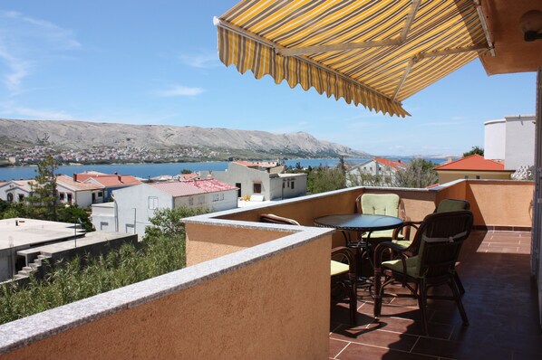 Une terrasse avec une table et des chaises, donnant sur un plan d’eau et une ville.