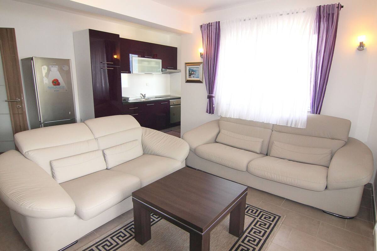 A living room with two beige sofas, a wooden coffee table, and a kitchen in the background.