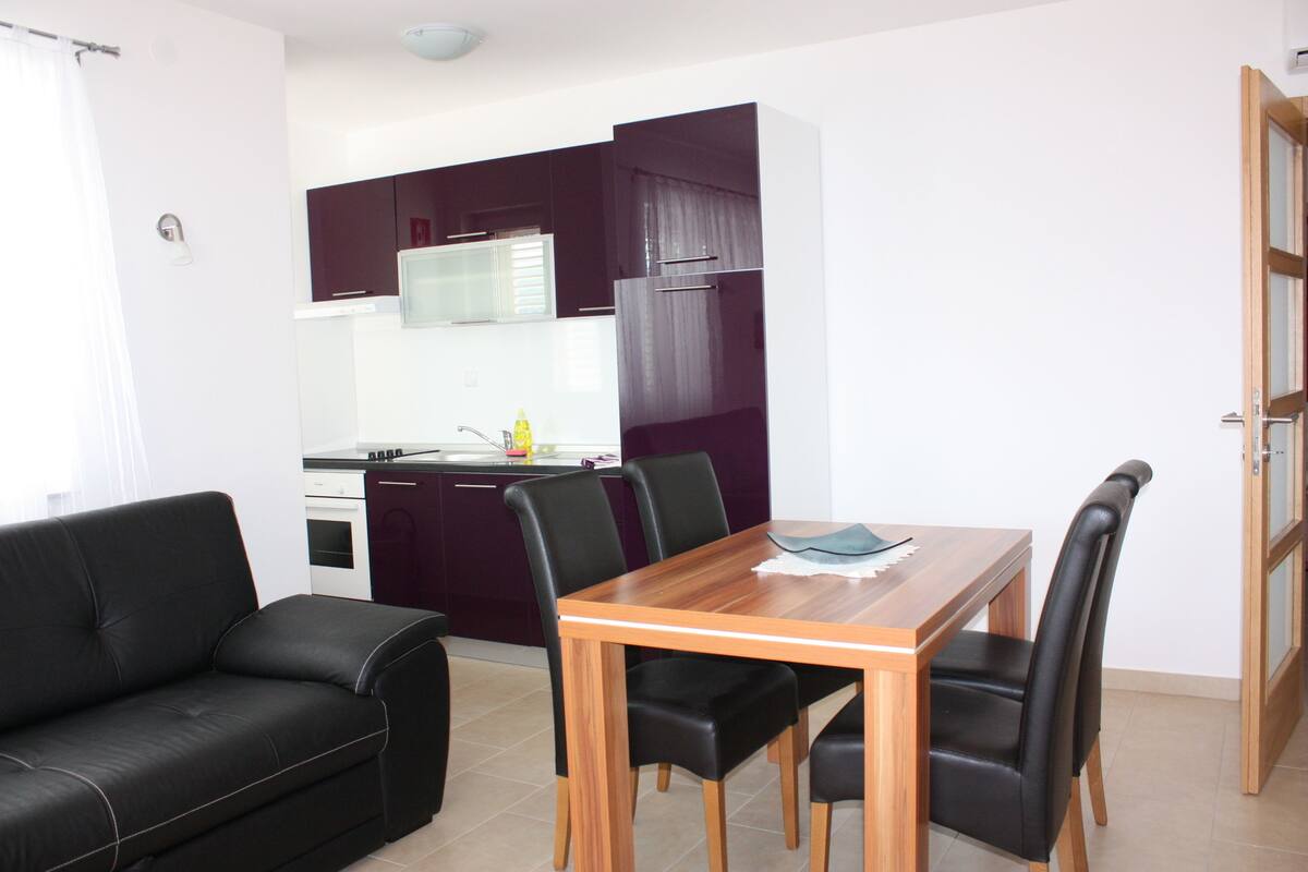 A compact living space with a kitchenette, a dining table with chairs, and a black leather sofa.