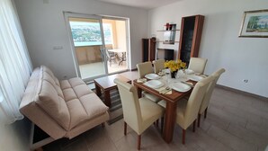 Uma área de refeições com mesa posta para quatro pessoas, um sofá e vista para uma varanda com mobiliário de exterior.