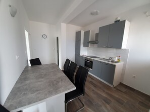 A modern kitchen with grey cabinets, a built-in oven, and a sink. There is a dining area with a grey table and black chairs.
