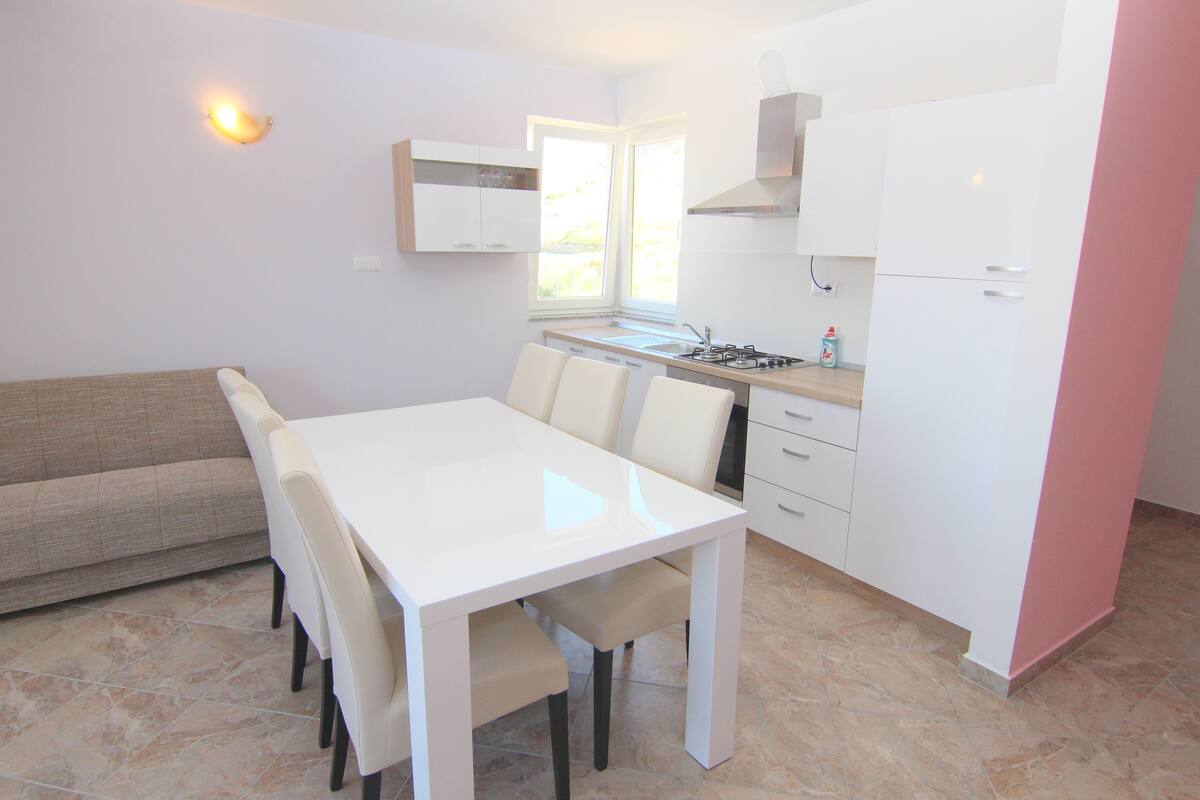 A modern kitchen with white cabinets, a dining table with chairs, and a built-in oven.