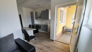 A modern living room with a grey sofa and a dining area with a table and chairs. - Apartments Ljubic (Pag)