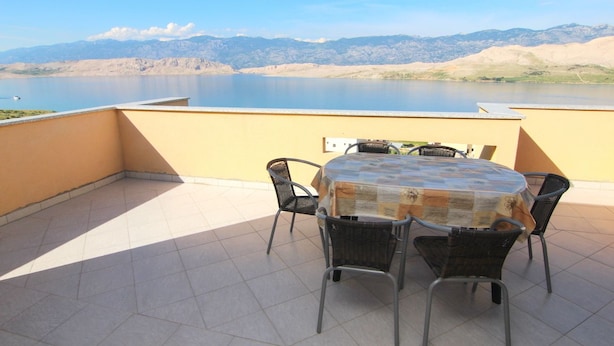 A round table with four chairs on a tiled patio overlooking a lake with mountains in the background. - Apartments Ljubic (Pag)