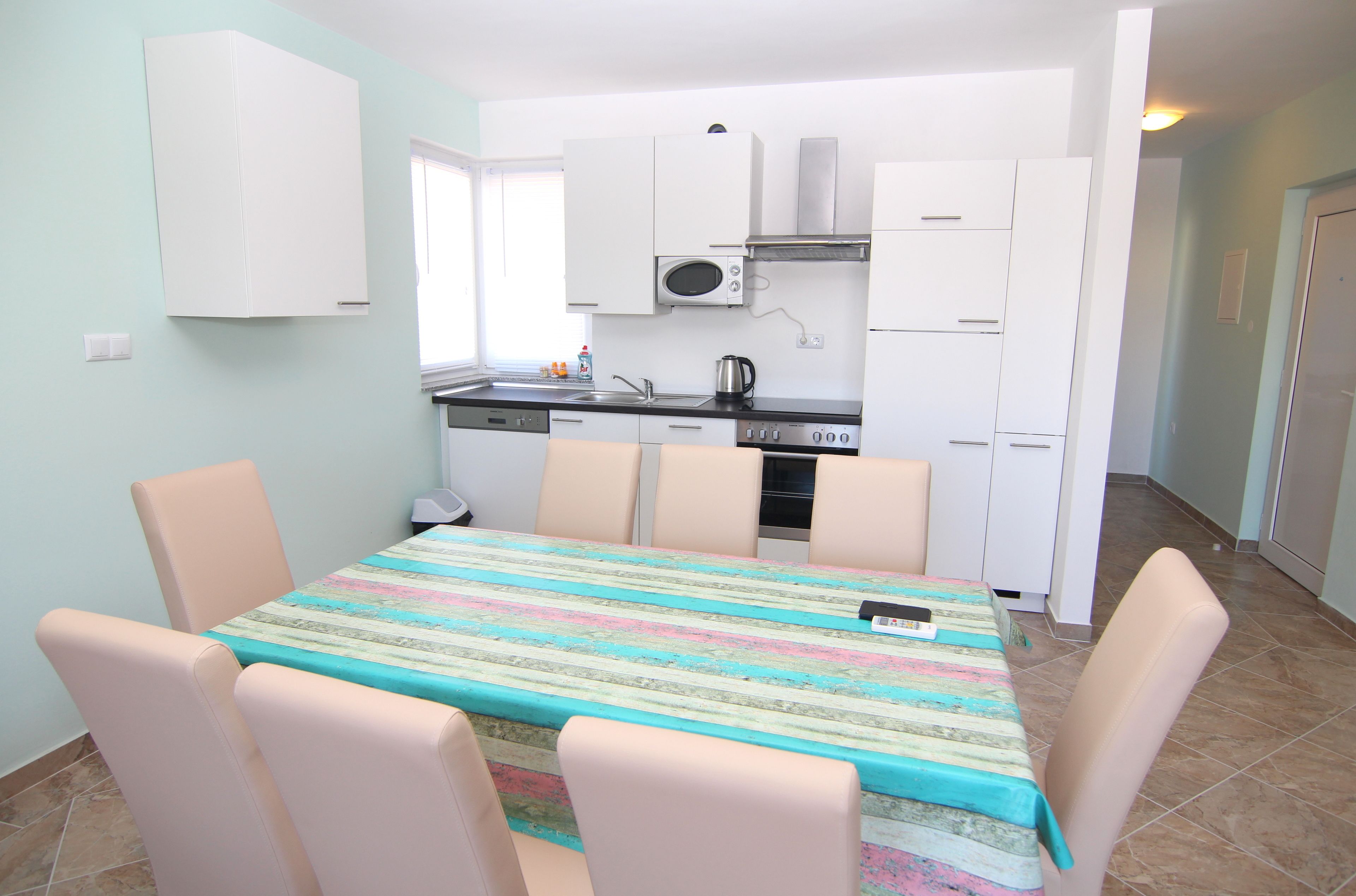 Cocina pequeña con armarios blancos, microondas y pileta. Hay una mesa de comedor con sillas y mantel colorido.