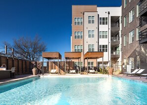 Une piscine entourée de bâtiments à plusieurs étages dotés de balcons, avec des chaises longues et une pergola à proximité.