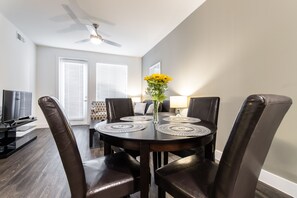 Un coin repas avec une table ronde, quatre chaises, un vase rempli de fleurs jaunes et un ventilateur de plafond.