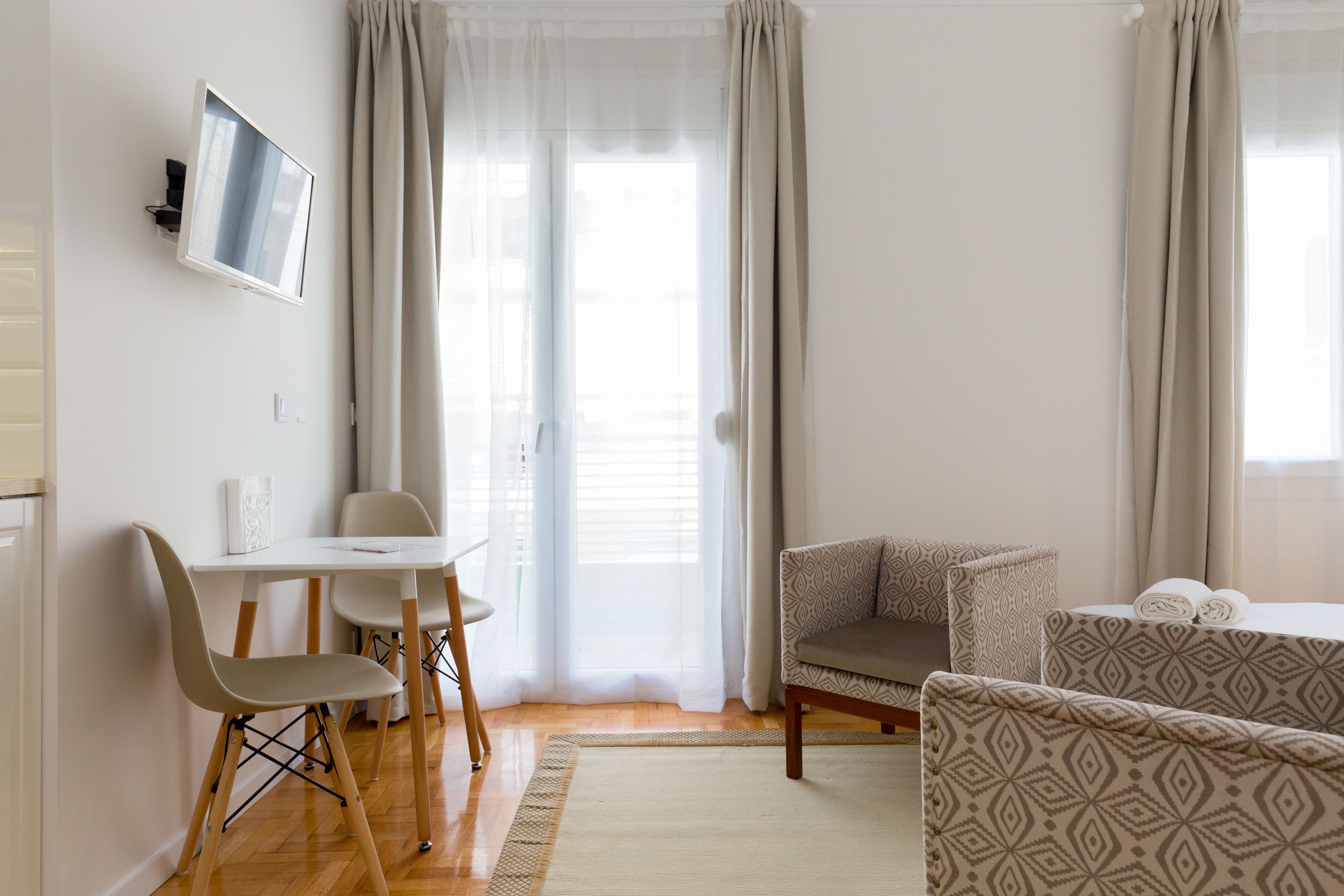 Una sala de estar moderna y bien iluminada con un televisor de pantalla plana en la pared, un comedor con mesa y sillas, y un sofá con cojines estampados.