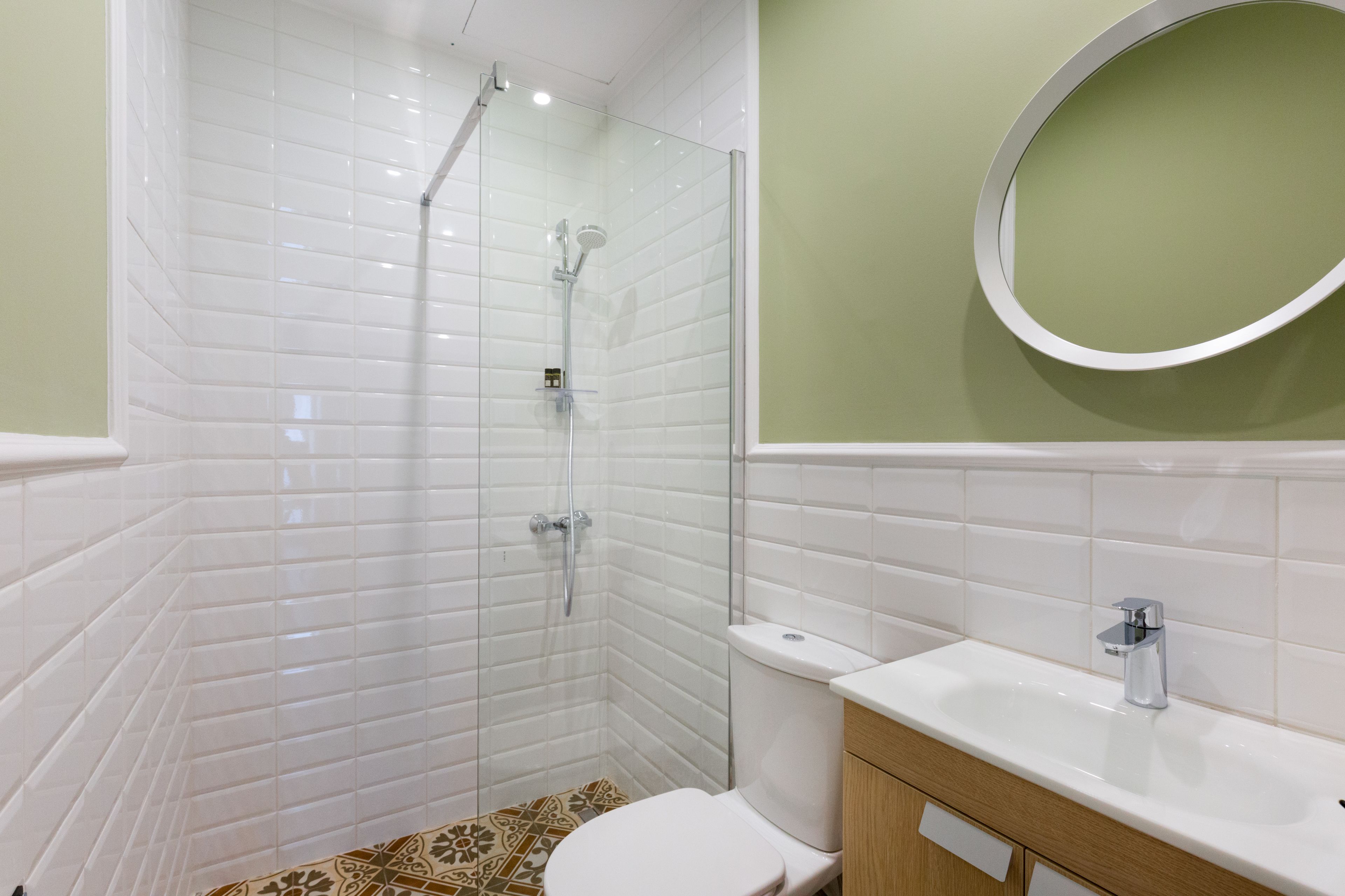 A modern bathroom with white tiles, a glass-enclosed shower, a toilet, and a sink with a mirror.