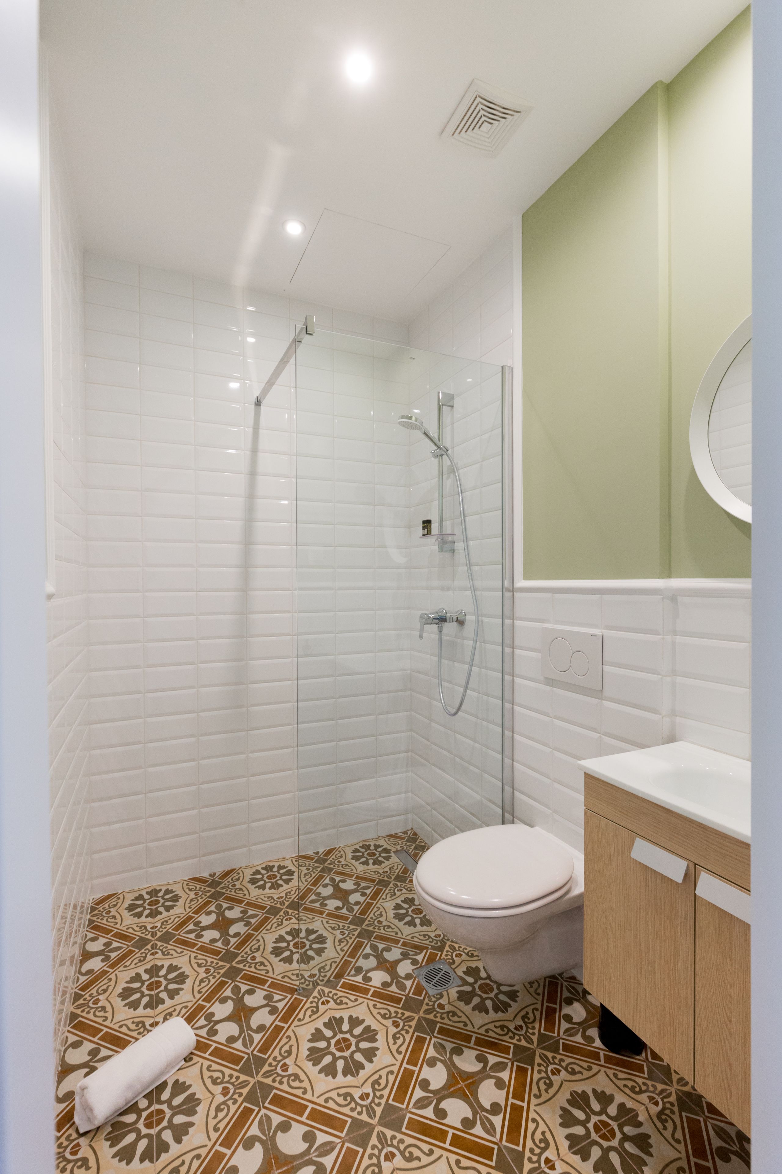A bathroom with white tiled walls, a shower with a glass door, a toilet, and a sink with a wooden cabinet.