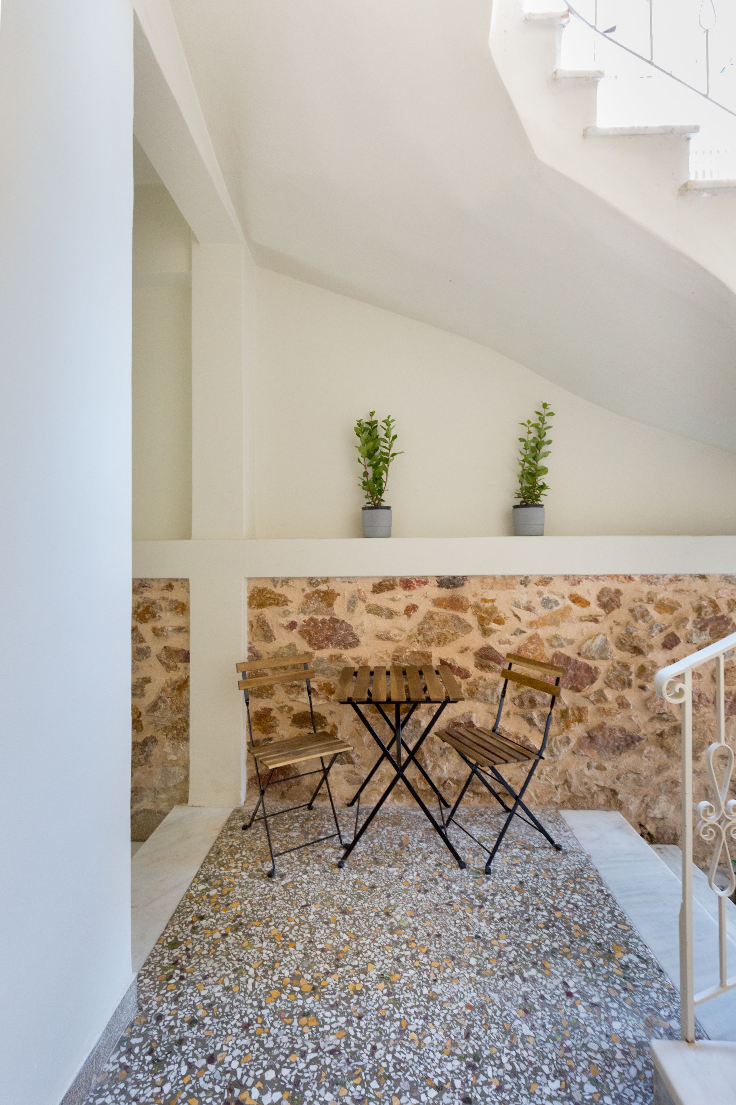 Eine Treppe mit einer Steinsäule und einem Terrazzo-Boden, die zu einer Zwischenebene mit einer Bank und zwei Topfpflanzen führt.