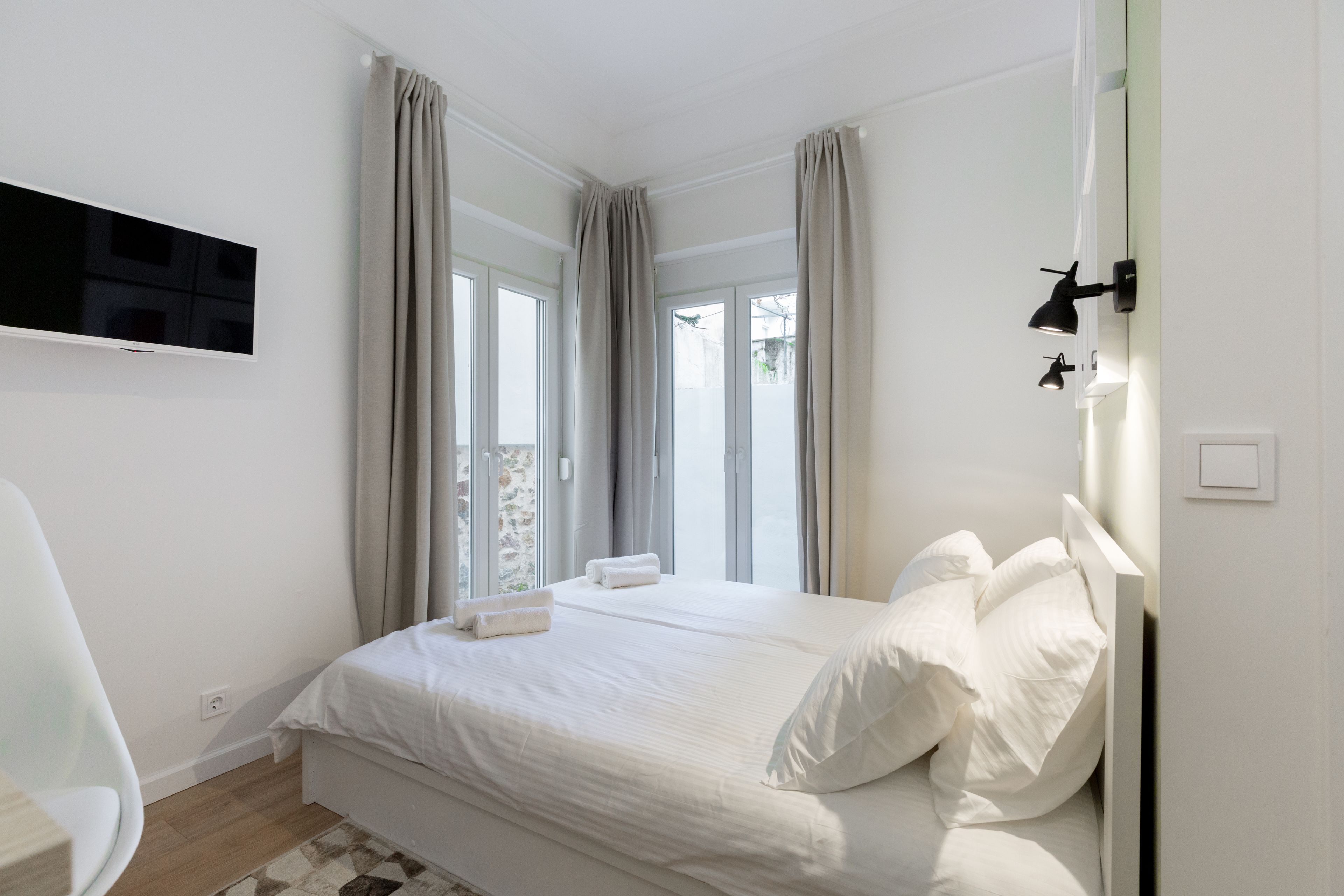 A bedroom with a bed, a TV mounted on the wall, and a window with curtains.