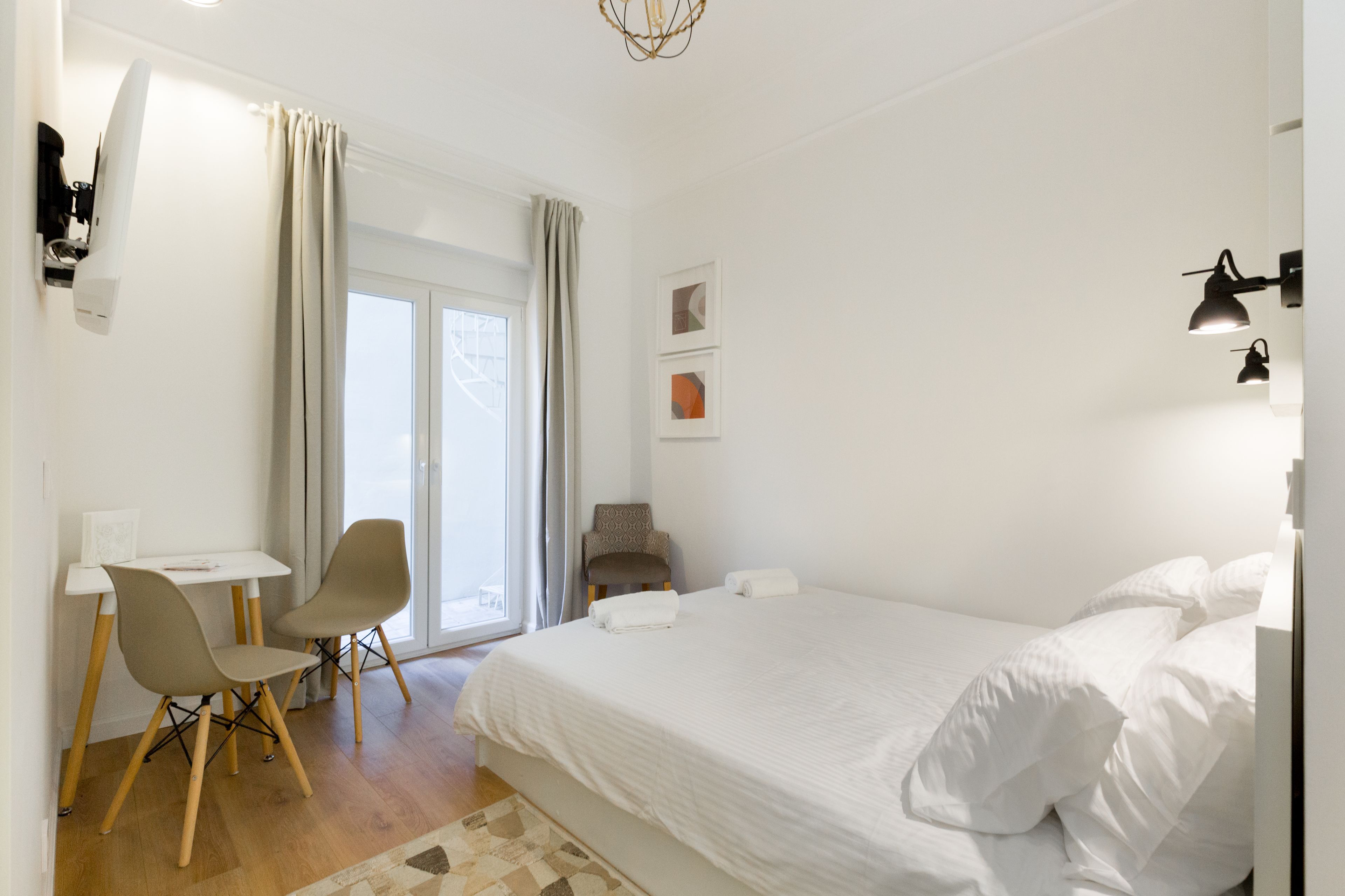 Une chambre à coucher avec un grand lit, un bureau avec deux chaises, un fauteuil et une fenêtre avec des rideaux.