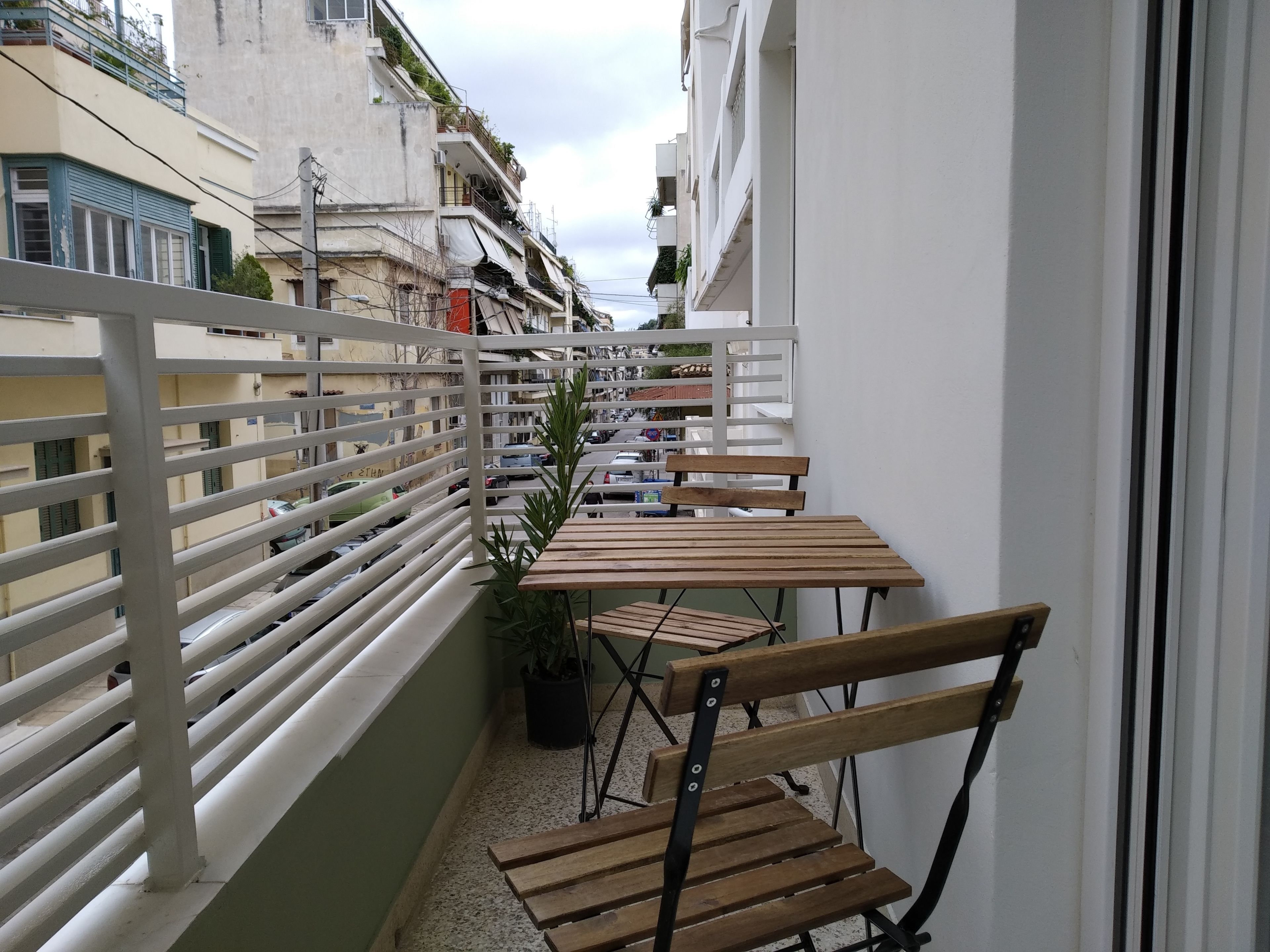 A balcony with a wooden table and chairs, a potted plant, and a white railing.