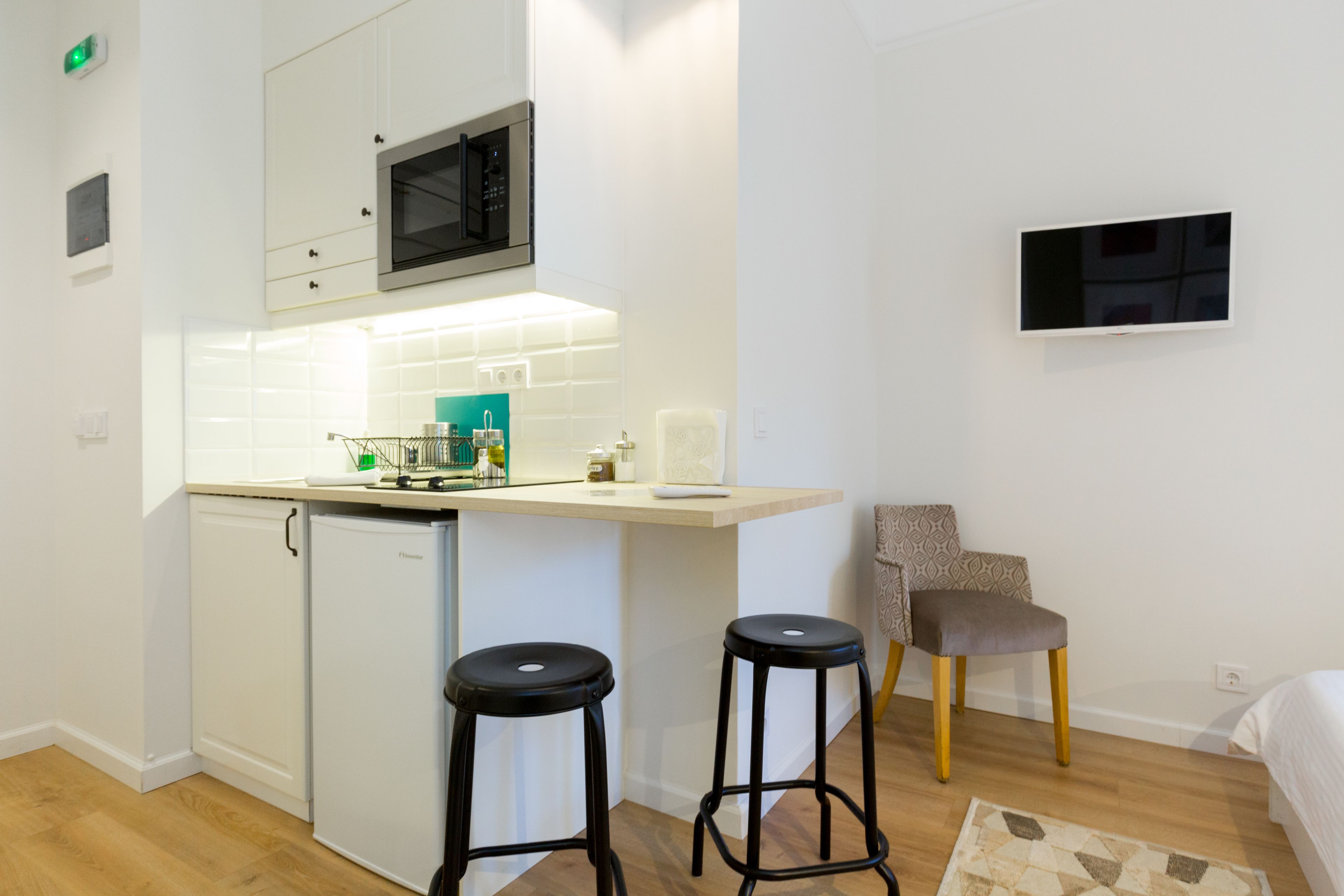 A compact kitchen with a microwave, a small refrigerator, and a bar stool.