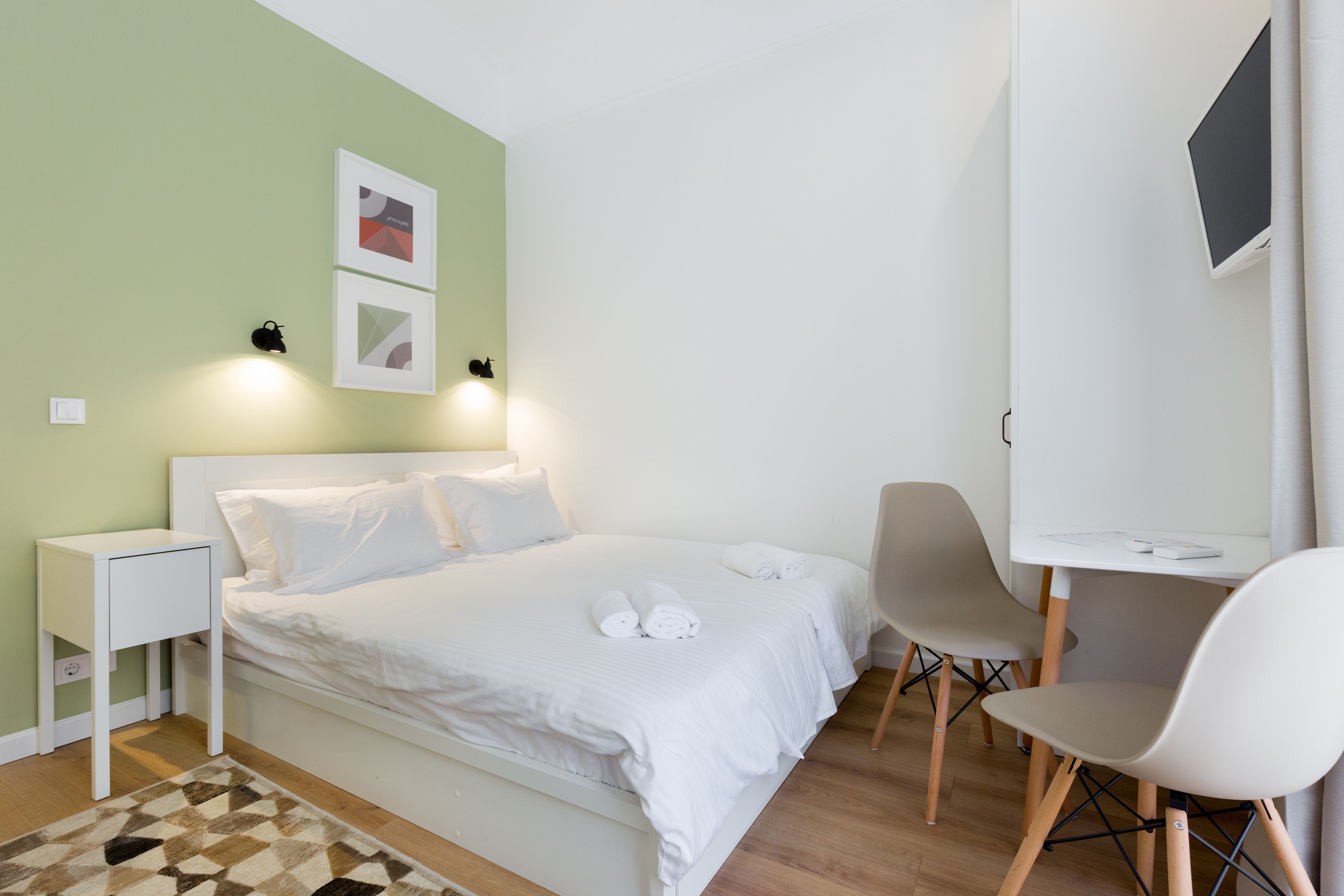 A neatly arranged bedroom with a bed, bedside table, and a desk with a chair.