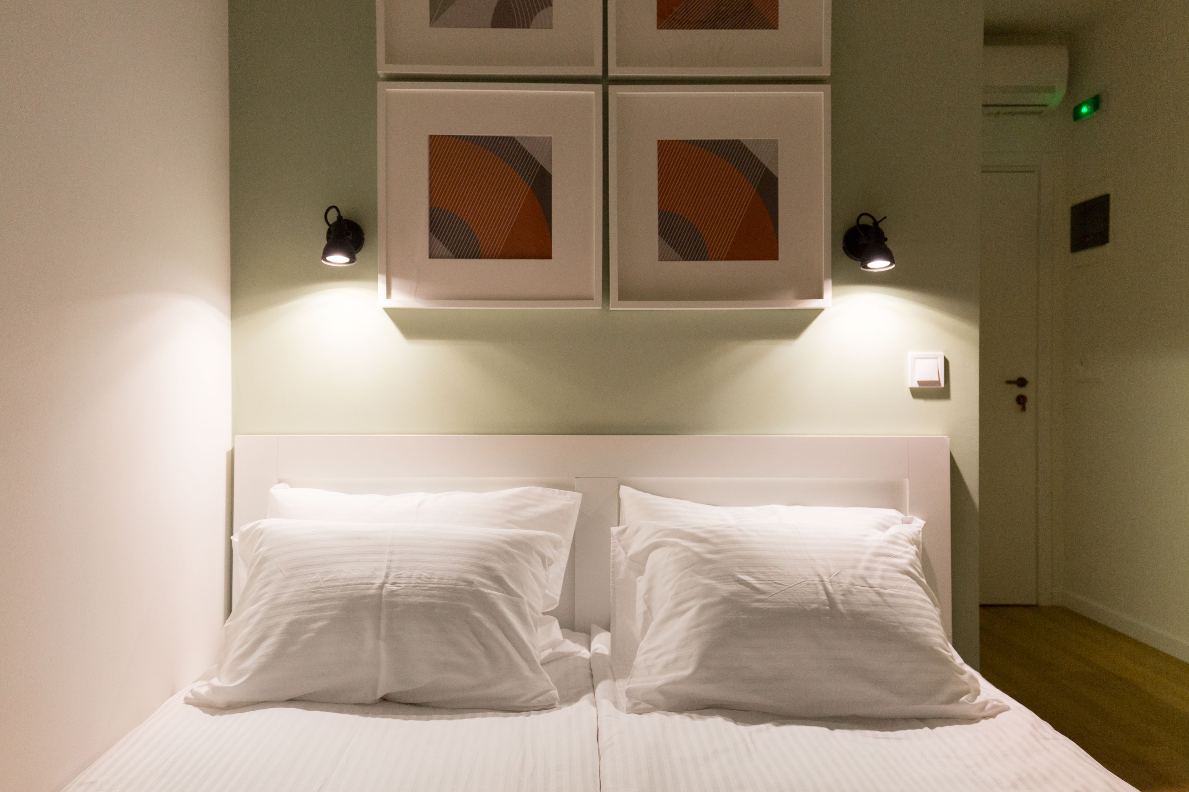 A neatly made bed with white linens and two pillows, a headboard, and wall-mounted light fixtures.