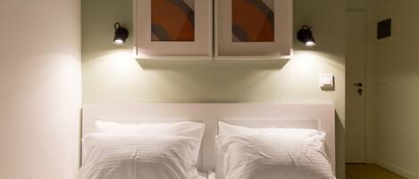 A neatly made bed with white linens and two pillows, a headboard, and wall-mounted light fixtures.