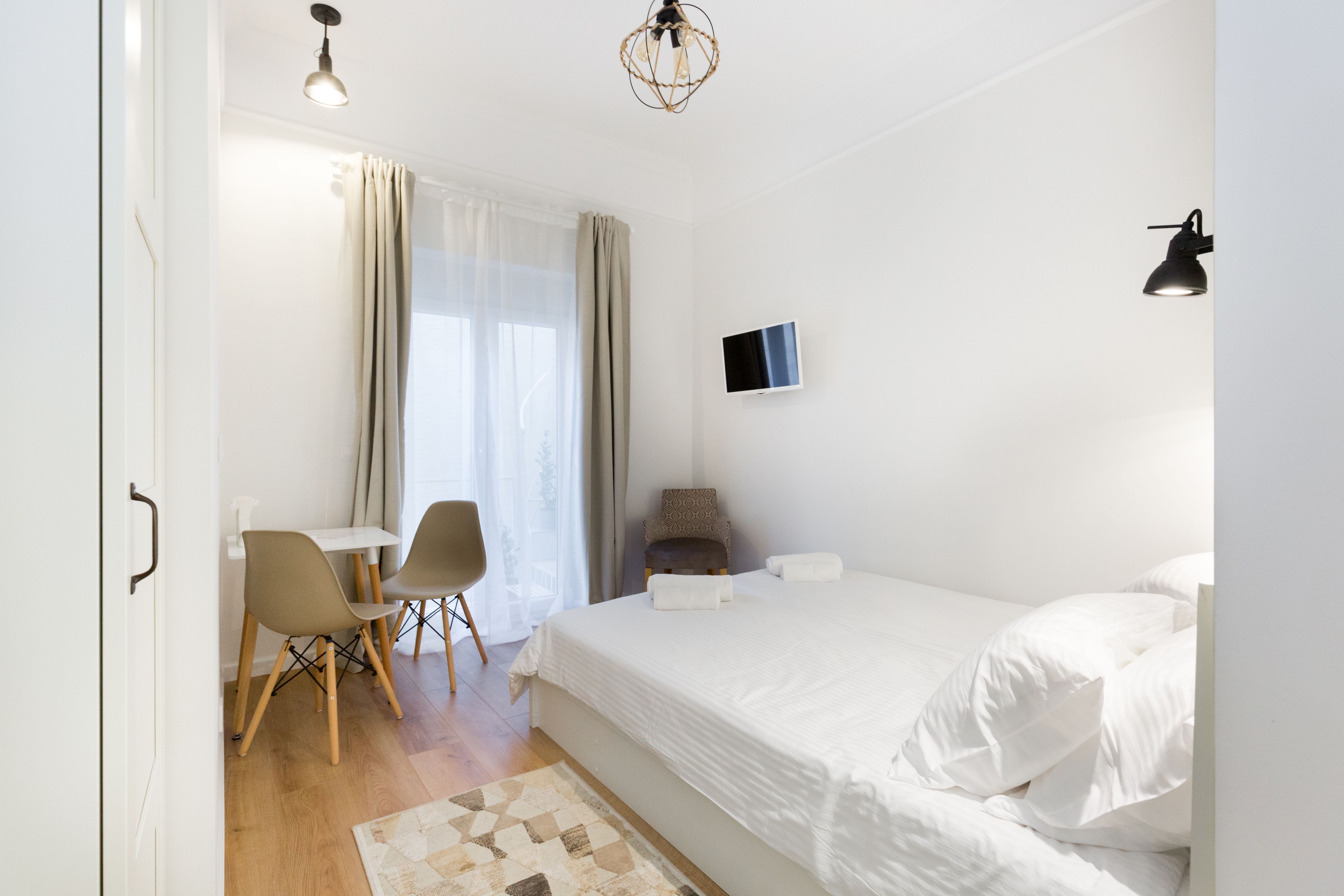 A modern hotel room with a large bed, a desk with two chairs, a TV, and a patterned rug.