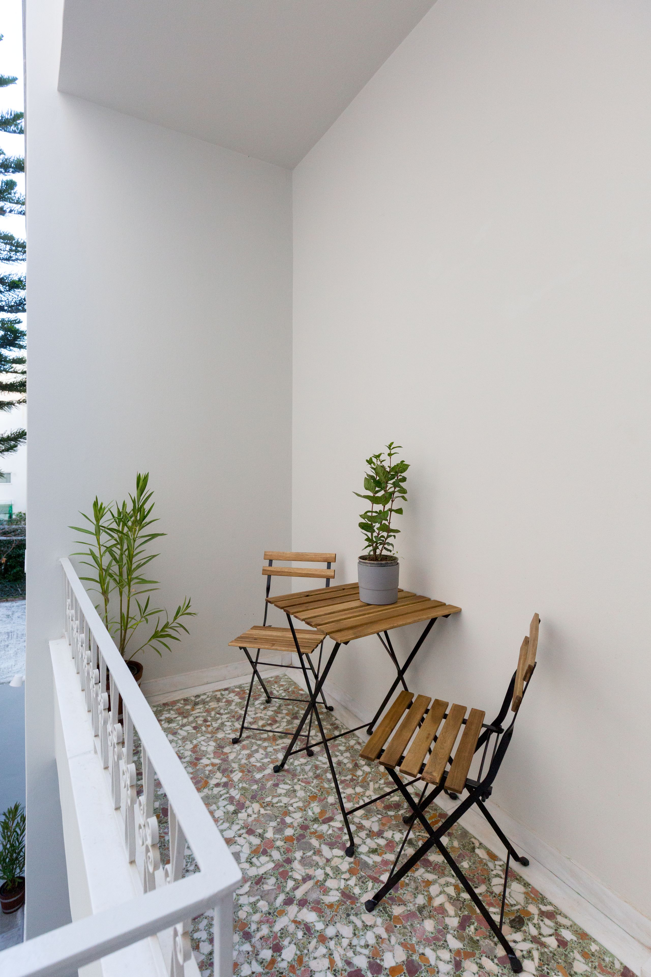 A balcony with a wooden table and chairs, a potted plant, and a white railing.