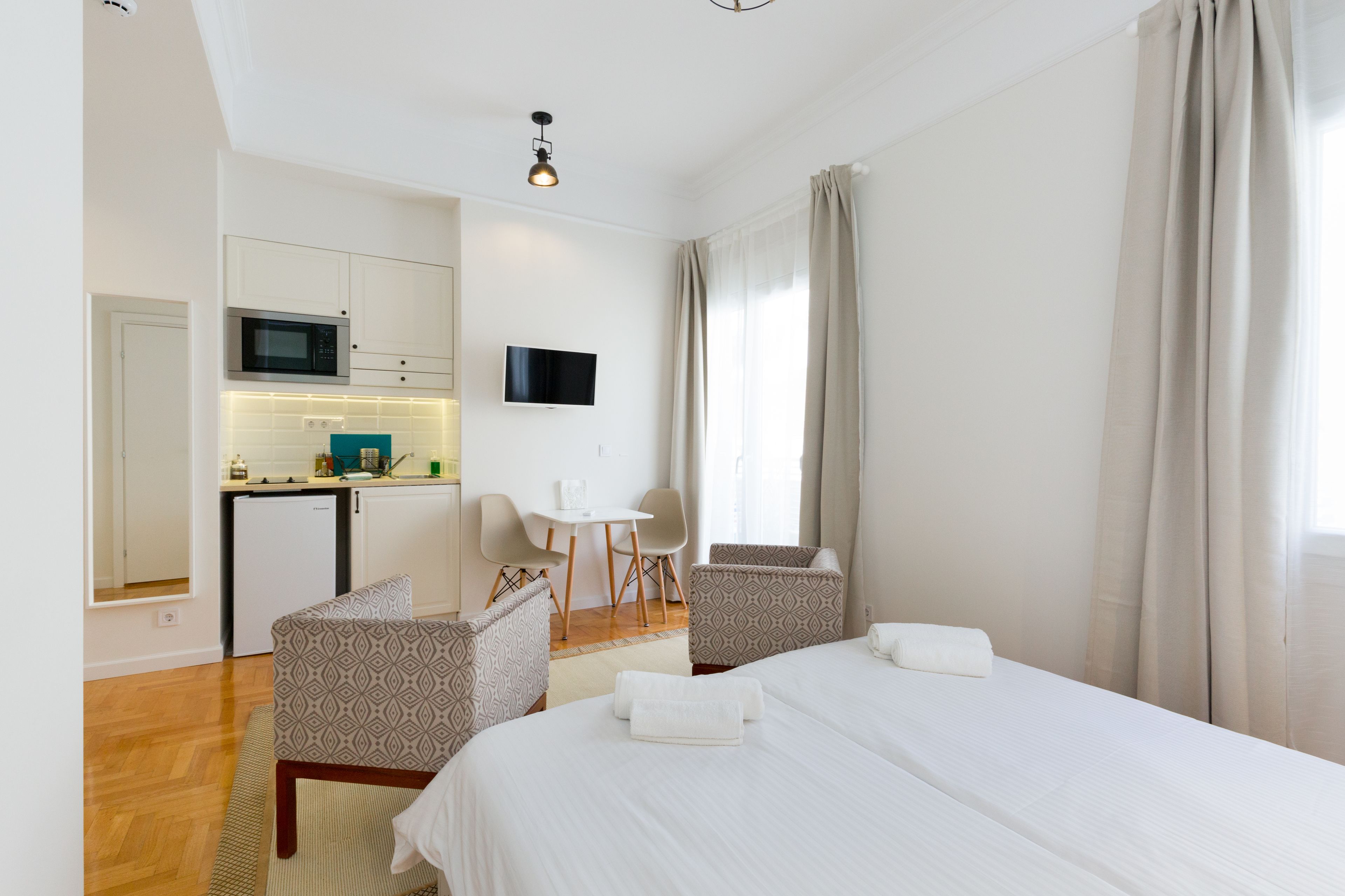 Habitació d'hotel moderna amb un llit, dues cadires amb un disseny decoratiu, una taula petita amb microones, un televisor i una finestra amb cortines.