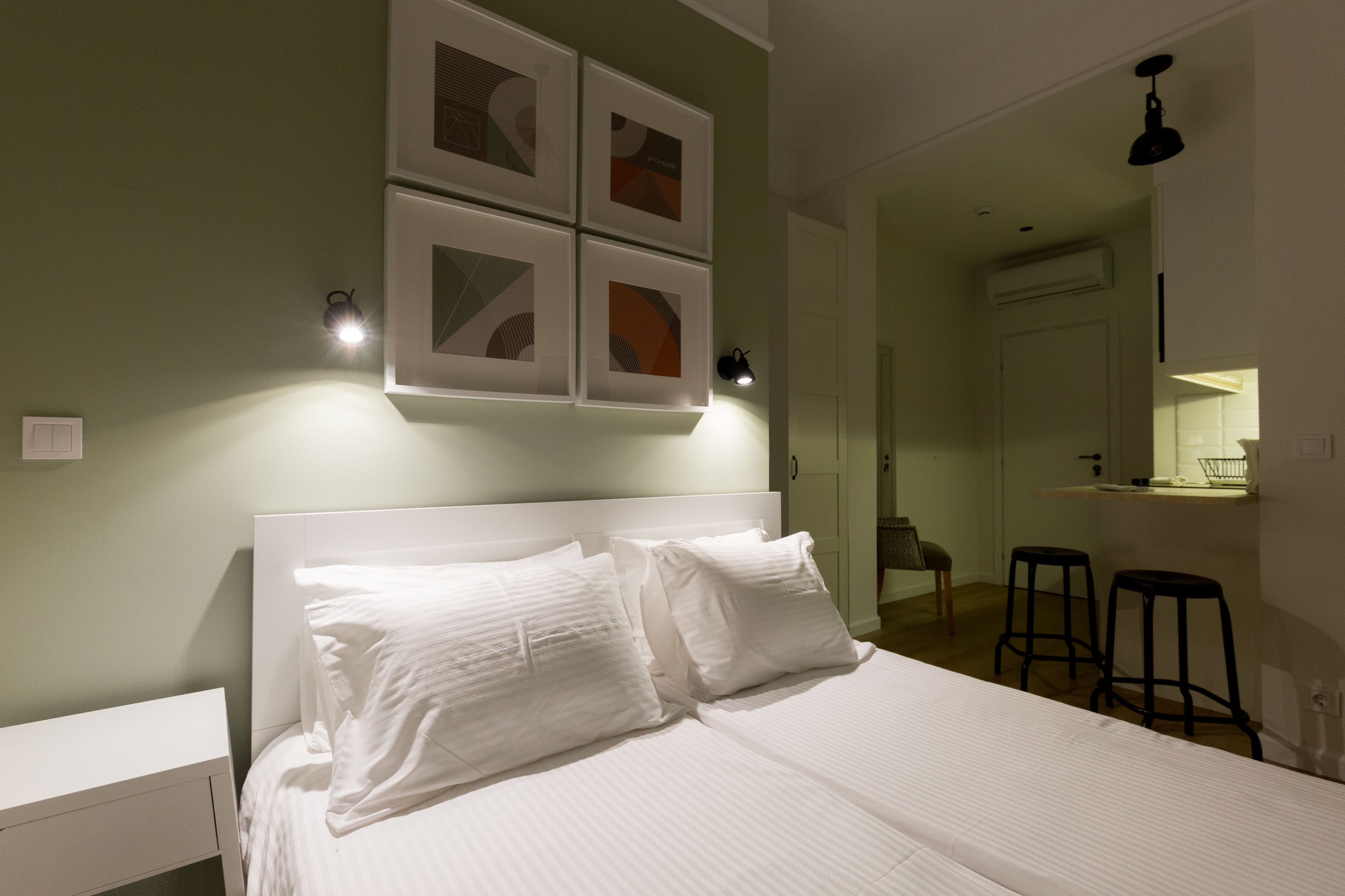 Un dormitorio ordenado con una cama grande, una mesita de noche y una lámpara auxiliar. Hay dos apliques y una lámpara de techo.
