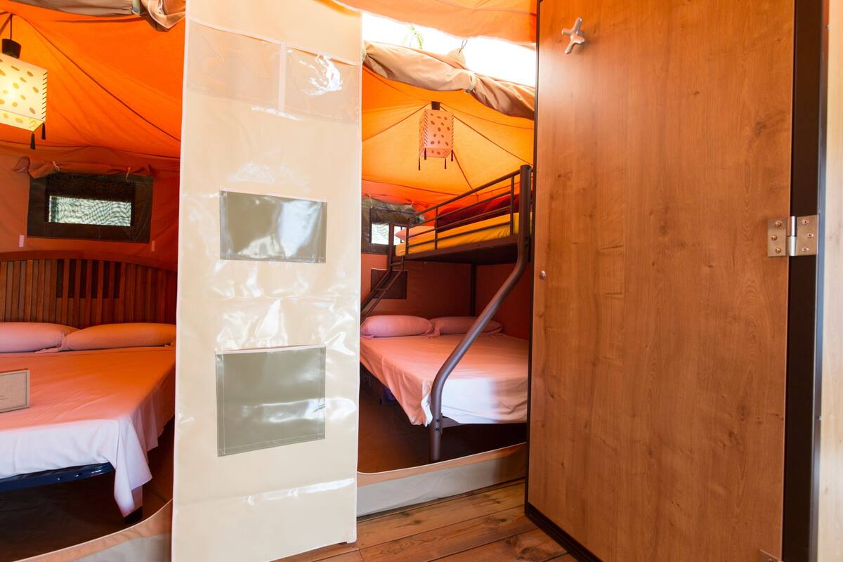 Habitación pequeña con literas, una puerta de madera y una ventana con persianas.