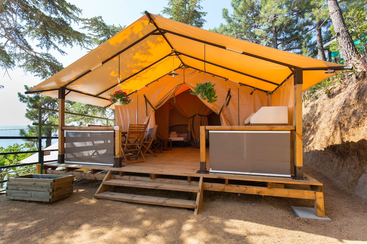 Una carpa con estructura de madera y un dosel, rodeada de árboles y vista al agua.